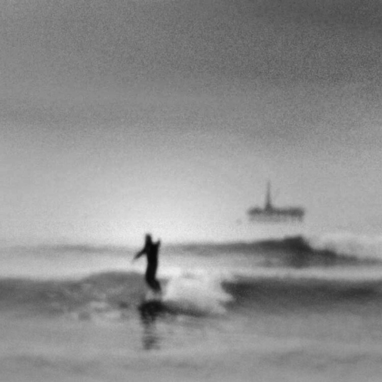 A blurry shot of artist Matt Beard surfing off the coast of Southern California with oil rig platform in the distance